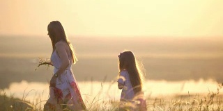 母亲和女儿在日落时分在山上采花编花环