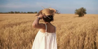 一个美丽的女孩穿着白色的夏装，戴着草帽在麦田里自由奔跑。背后的观点