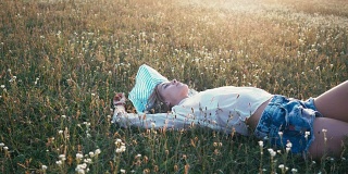 美丽微笑的女孩躺在春天的田野上。草地。微笑和快乐的年轻模特的肖像与健康的长发吹享受自然。户外美女