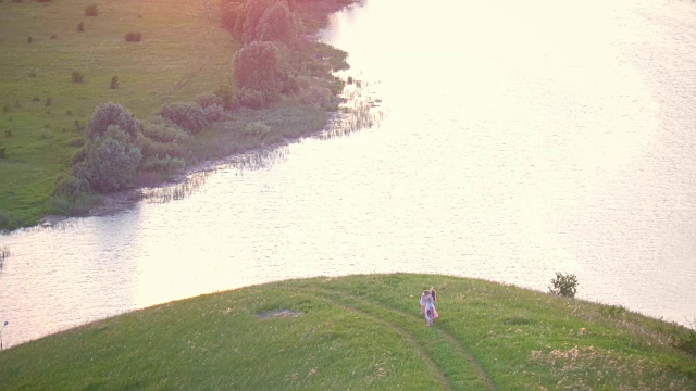 鸟瞰图-母亲和女儿在夏天日落时河边的小山上玩耍