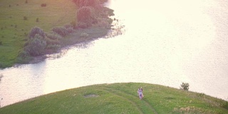 鸟瞰图-母亲和女儿在夏天日落时河边的小山上玩耍