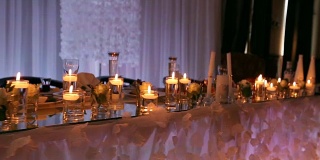 婚礼宴会厅的内部细节与装饰餐桌设置在餐厅。蜡烛和白色花瓣装饰玫瑰花在玻璃花瓶装满水