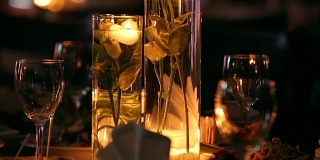 婚礼宴会厅的内部细节与装饰餐桌设置在餐厅。蜡烛和白色花瓣装饰玫瑰花在玻璃花瓶装满水