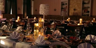 夹包,序列。婚礼宴会厅的室内细节与餐厅的餐桌布置相结合。蜡烛和白色花瓣用玫瑰装饰在玻璃花瓶里
