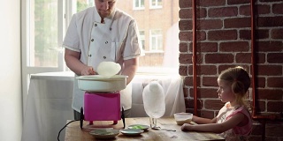 一个男厨师在一个特殊的机器上为一个可爱的小女孩制作棉花糖。