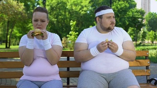 肥胖的年轻夫妇吃汉堡，沉迷于垃圾食品，缺乏意志力视频素材模板下载