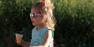 在一个阳光明媚的夏日，一个小女孩戴着太阳镜吃冰淇淋。