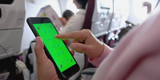 近距离女人手向上滚动绿色屏幕的手机应用在飞机座位上