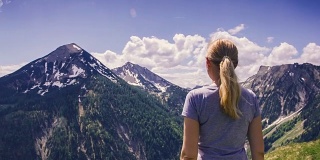 年轻女子举起双手站在背后的山上。