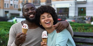 快乐的男朋友和女朋友在长椅上笑着，浪漫的约会吃着冰淇淋