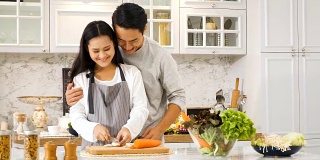 年轻的亚洲孕妇和丈夫在厨房做饭在家
