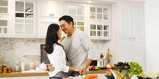 年轻的亚洲孕妇和丈夫在厨房跳舞