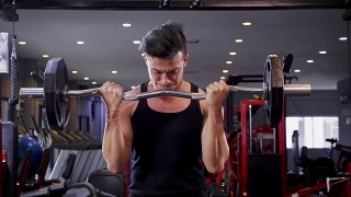 年轻的健身男子做二头肌卷曲与E-Z酒吧在健身房，健身训练的概念视频素材模板下载