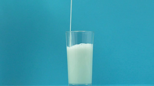 新鲜牛奶倒在玻璃上，蓝色背景，钙和磷的来源