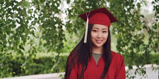 这是一幅迷人的亚洲女孩成功毕业的照片，她穿着学士服站在校园里，微笑着看着镜头。青年教育理念。