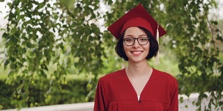 这是一幅快乐的年轻女毕业生的照片，她穿着学士服，面带微笑地站在校园的树下。青年教育理念。