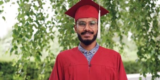这是一幅长着大胡子的混血学生的肖像，他身着学士服，面带微笑地站在校园外看着摄像机。人与教育观念。