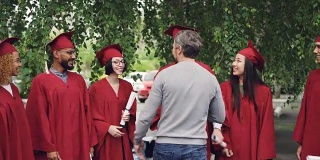 骄傲的父母在大学校园的背景下祝贺学生毕业，与他们握手拥抱，年轻人在交谈和微笑。