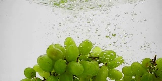 一串绿葡萄掉进水里，慢镜头里还带着泡泡。白色背景上的浆果。