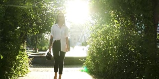 时尚的年轻女子高跟鞋在公园散步在喷泉的背景