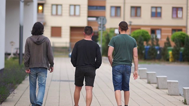 年轻人在城市里散步。后视图。三个人跑到远处。夏天散步，周末，假期