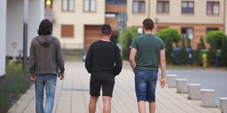 年轻人在城市里散步。后视图。三个人跑到远处。夏天散步，周末，假期