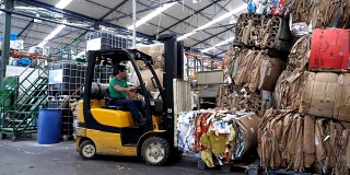 一名工人在回收工厂用叉车将回收的废品从一个地方运到另一个地方