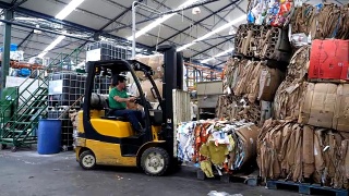 一名工人在回收工厂用叉车将回收的废品从一个地方运到另一个地方视频素材模板下载