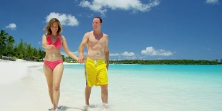 穿着泳衣的白人夫妇在沙滩上手拉手